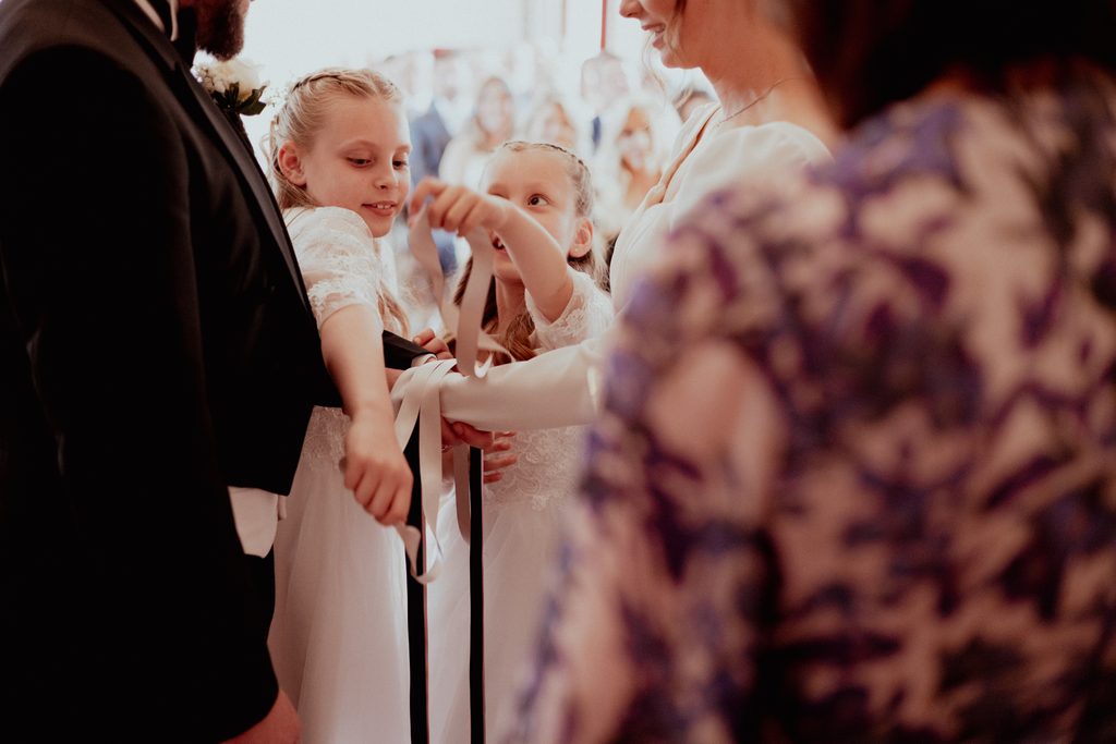 The children are included in a wedding ceremony by placing their ribbon as a symbol of their blessing.
