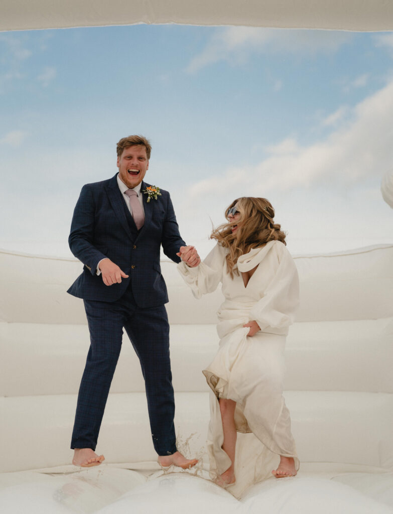Wedding couple bouncing on a whiten bouncy castle. They are laughing and having fun.